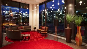 Un interior moderno con un sofá curvo, alfombra roja y grandes ventanales con vistas a la ciudad.