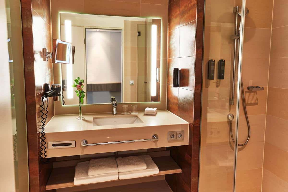 A modern bathroom with a large mirror, sink, and shower.