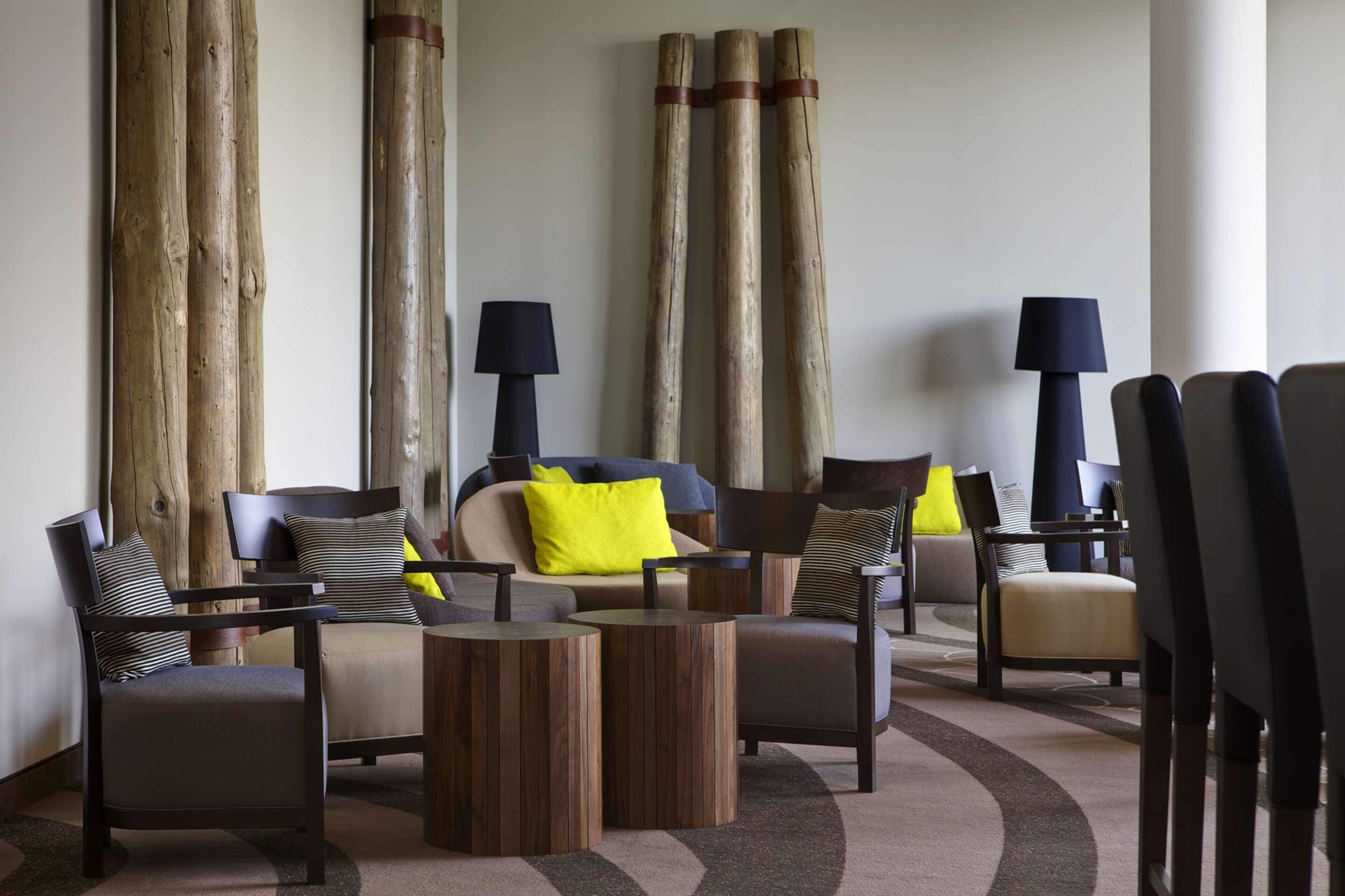 A modern living room with a sofa, armchairs, and a coffee table. There are two lamps and a large window with curtains.