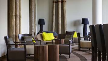 A modern living room with a sofa, armchairs, and a coffee table. There are two lamps and a large window with curtains.