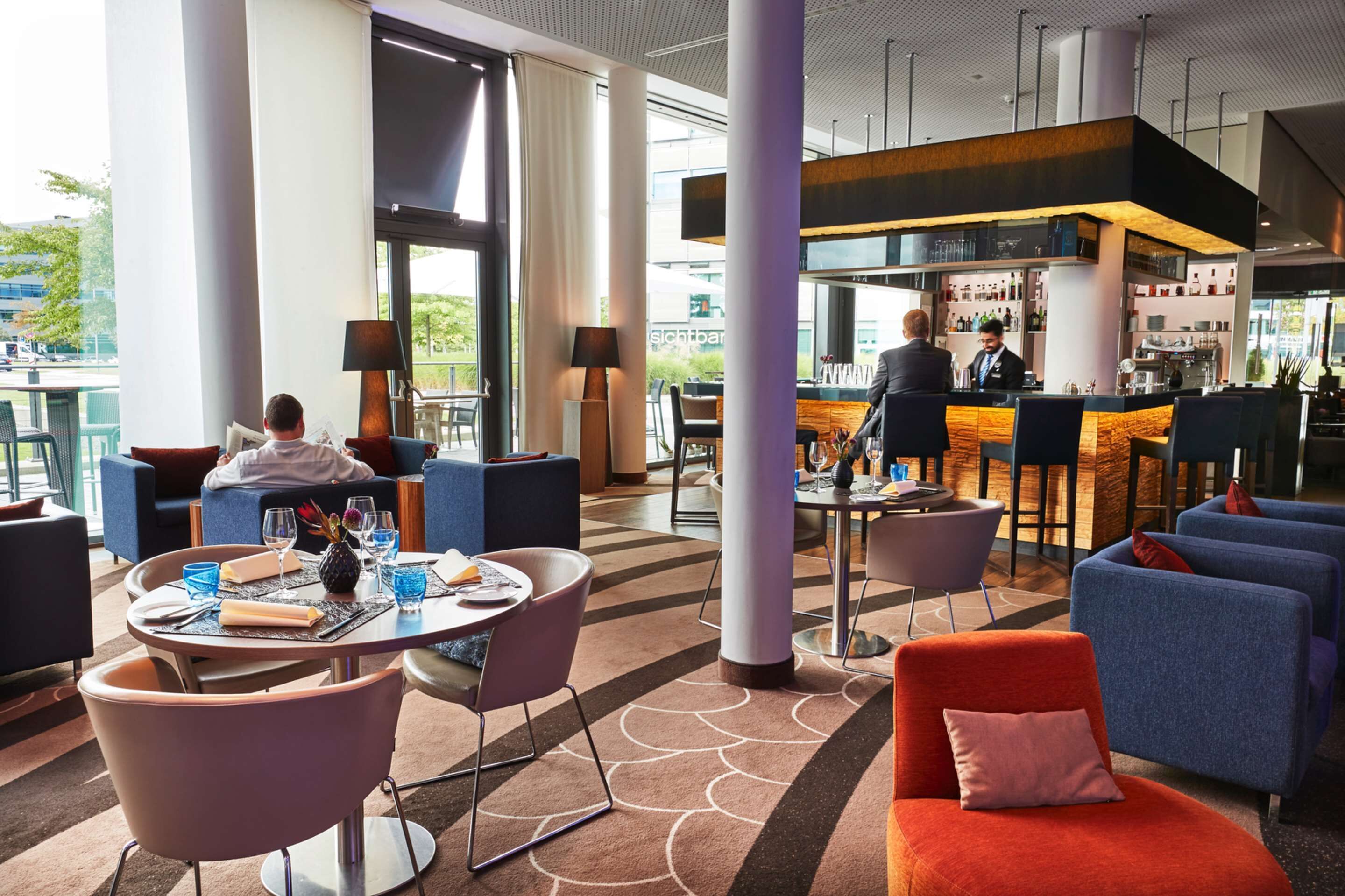 A modern hotel lobby with a bar area, seating arrangements, and large windows.