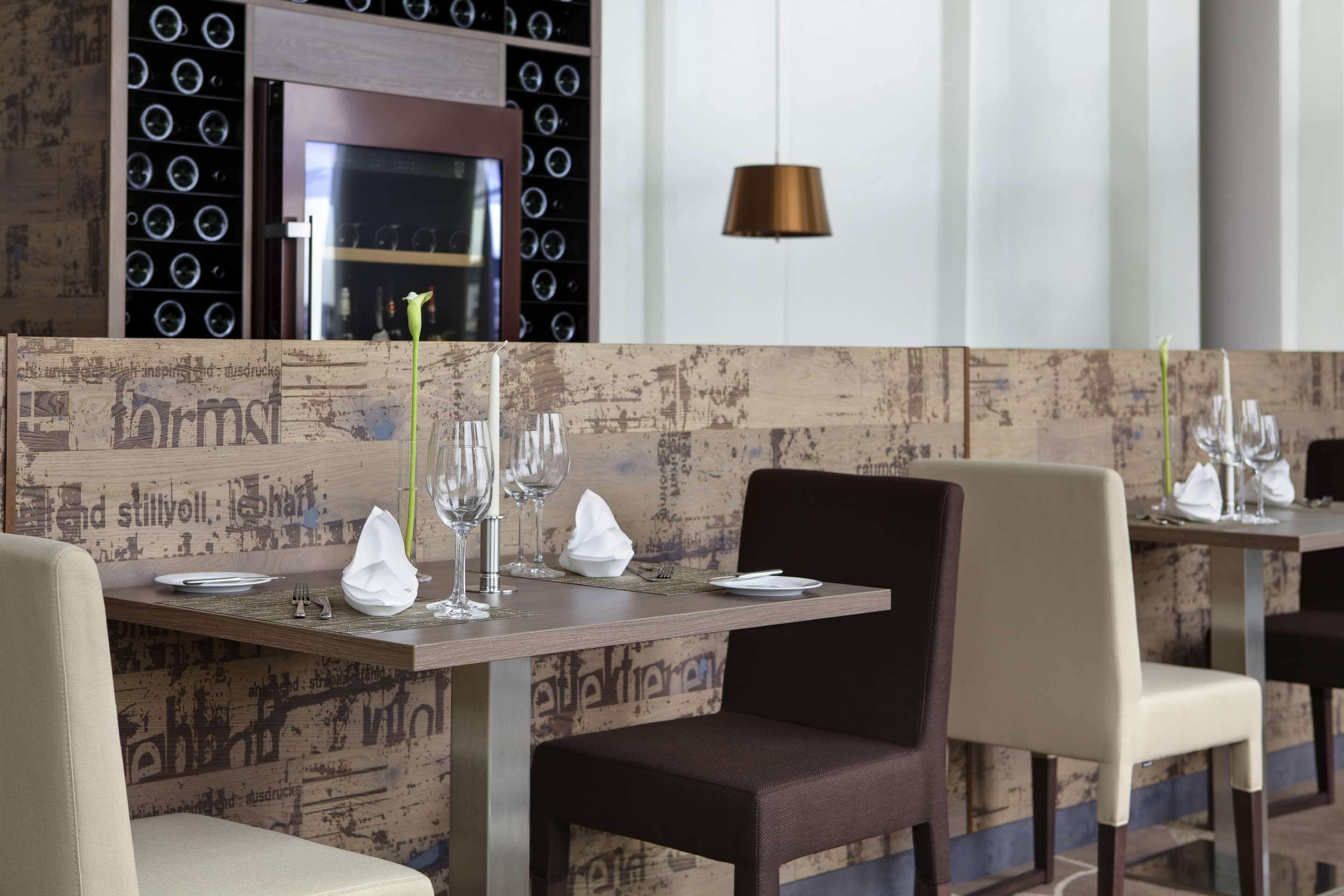 Ein Restaurant mit rustikaler Holzwand, ordentlich gedeckten Tischen und Stühlen sowie einer modernen Pendelleuchte.