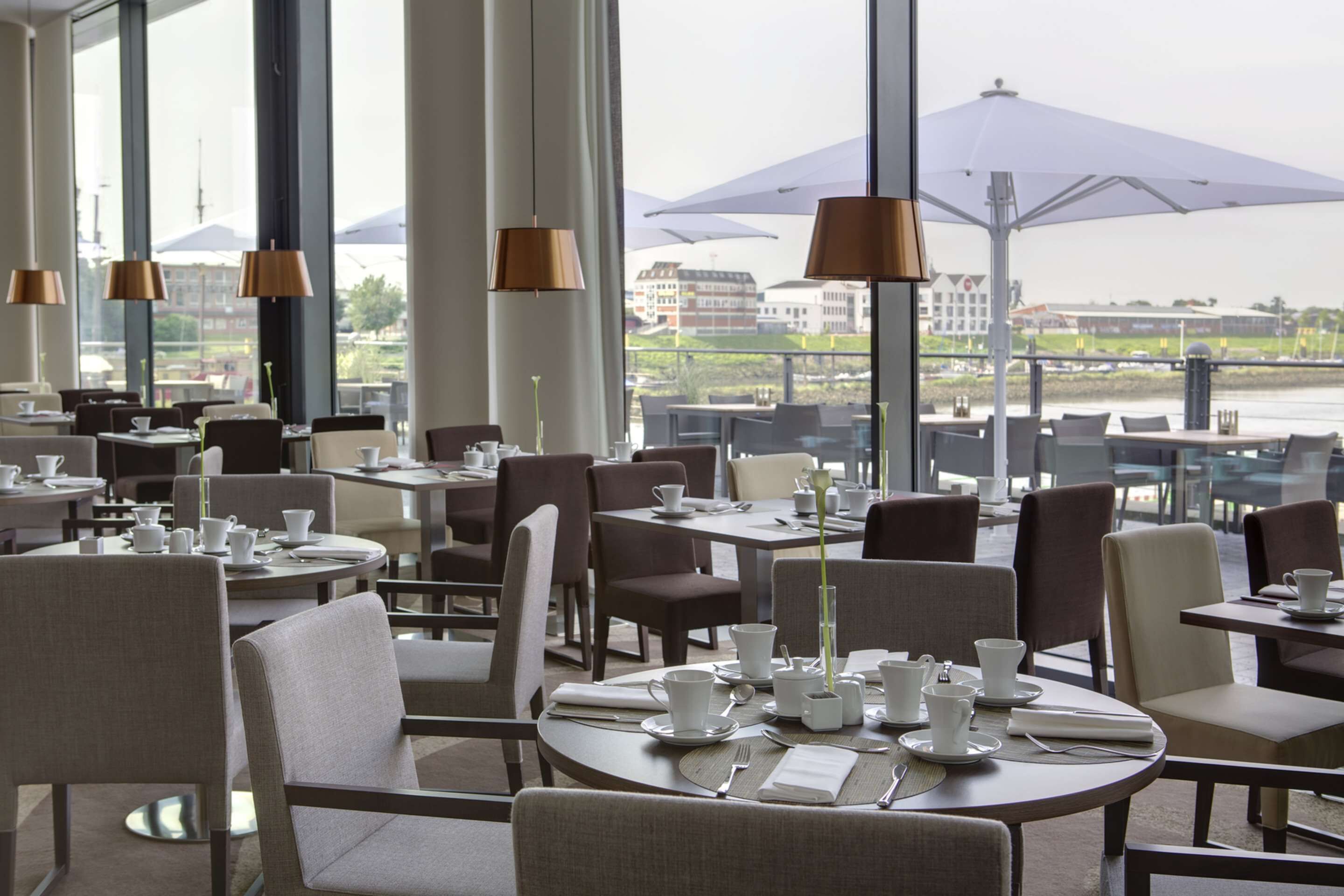 Een restaurant met ronde tafels en stoelen, grote ramen en parasols.