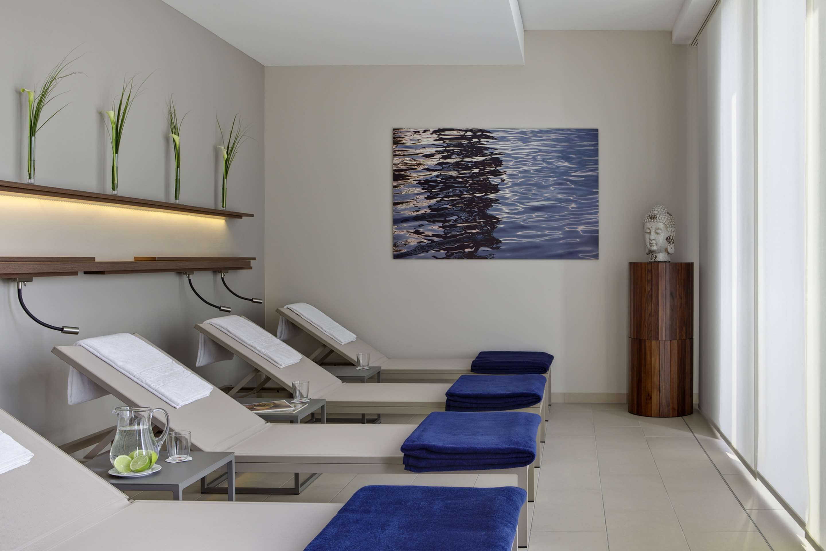 Un cuarto de spa con sillones reclinables, un cuadro de una playa y una estatua de Buda.
