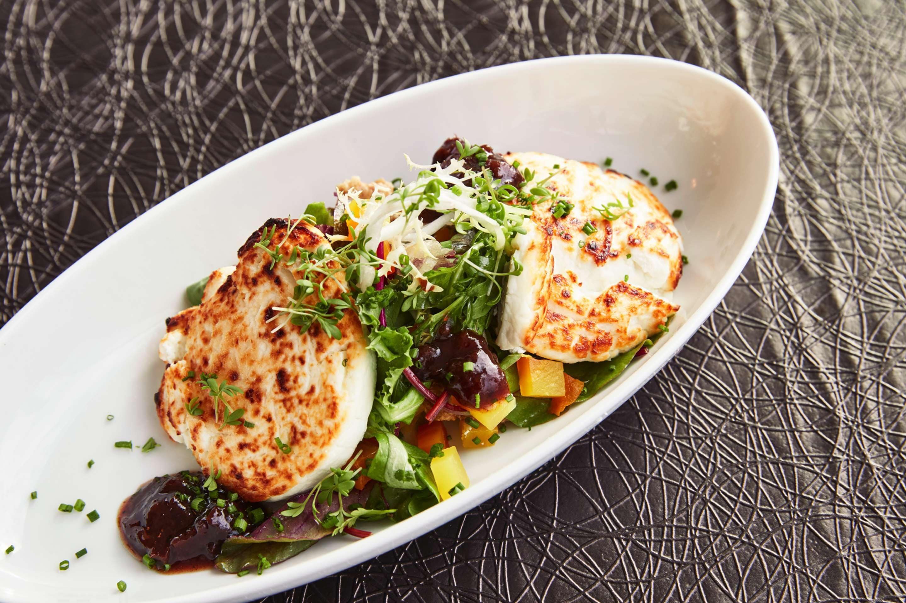 A white oval plate with grilled chicken, mixed greens, and cubed vegetables on a textured black surface.