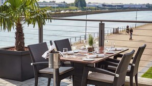 Un área de comedor al aire libre con sillas de mimbre y una mesa para dos, con vistas a un río.