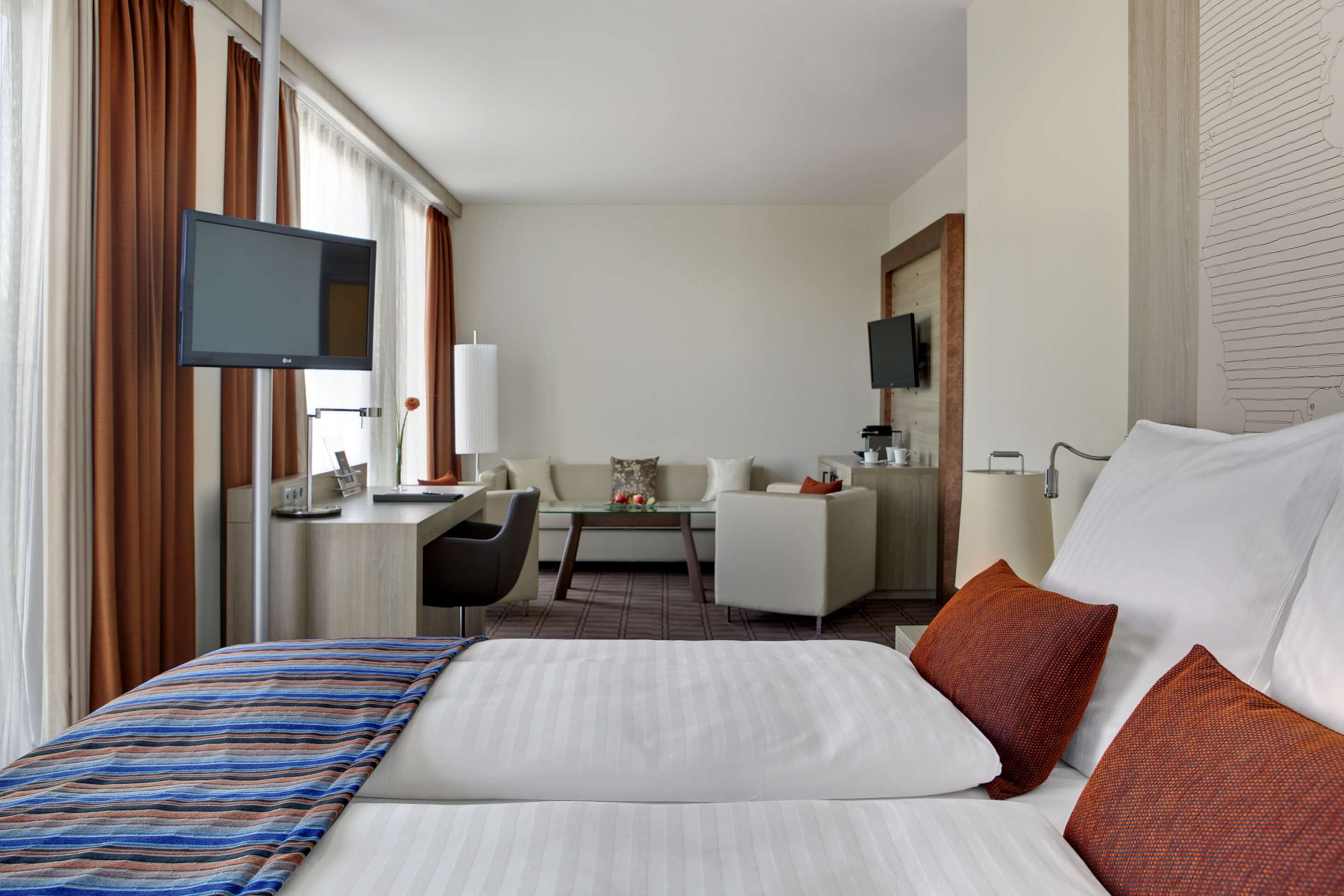 A hotel room with a bed, a desk, a chair, a TV, and a sofa.
