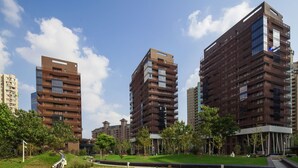A modern residential complex with multiple high-rise buildings, a landscaped park area with a skate park, and a clear blue sky.