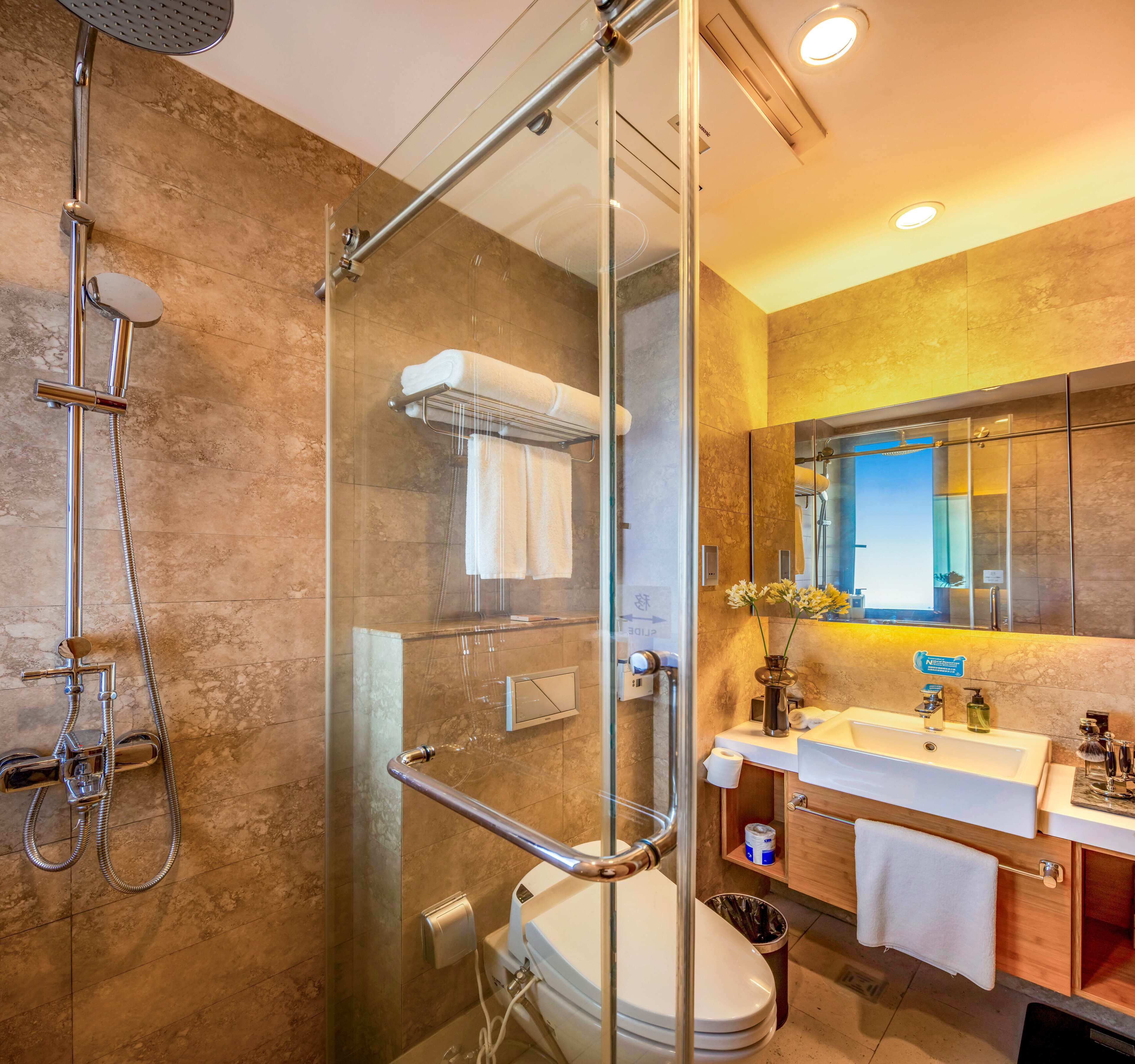 A modern bathroom with a glass-enclosed shower, a toilet, a sink with a mirror, and a trash can.