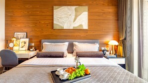A hotel room with a wooden wall, a bed with two pillows, a bedside table with a lamp, and a tray with food and drinks.