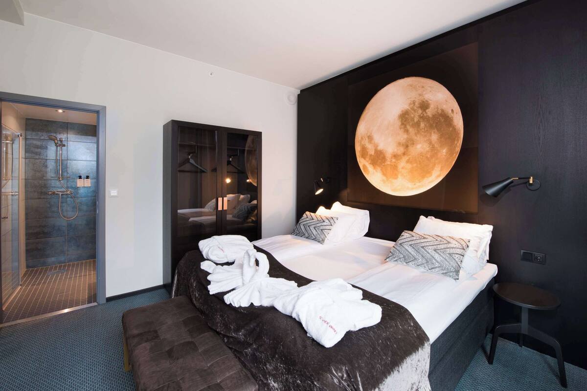 A modern hotel room with a large bed, a round wall clock, and a shower area.