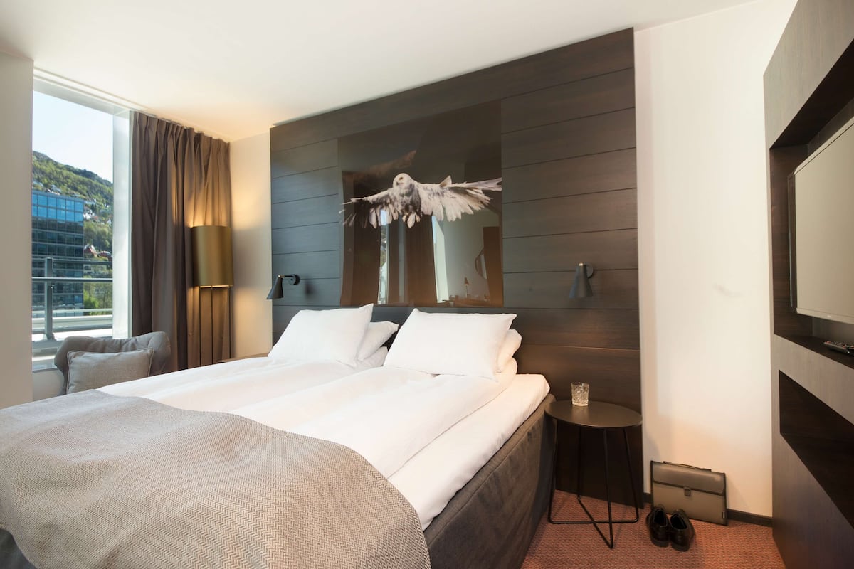 A modern hotel room with a large bed, a small side table, a chair, and a TV.