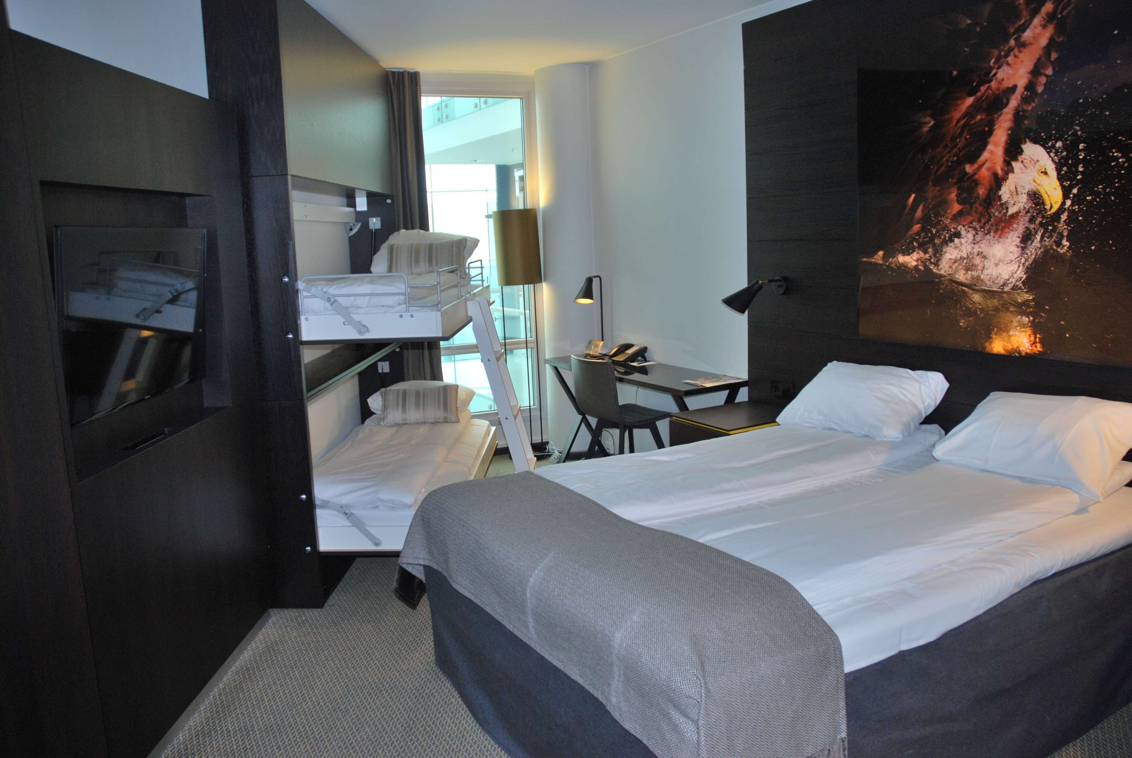 A hotel room with a large bed, a desk, a chair, and a small seating area.