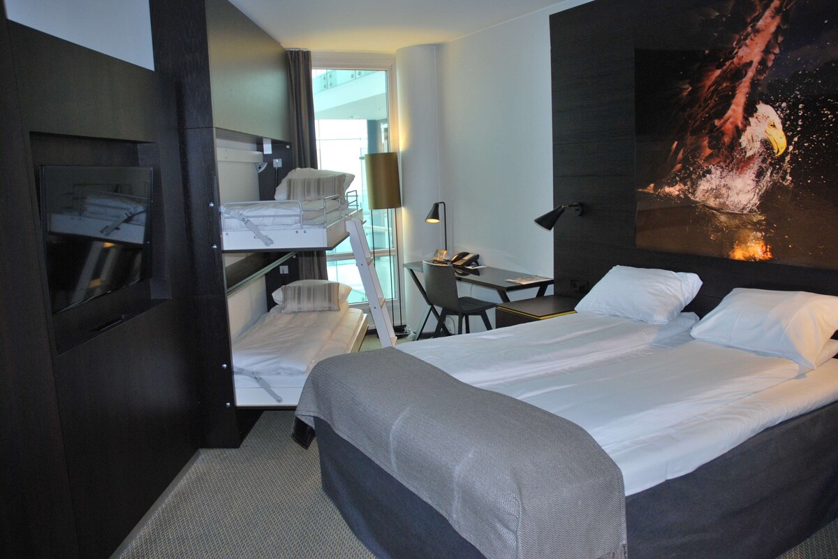 Una habitación de hotel con una cama, un escritorio, una silla, un espejo y un ventanal grande.