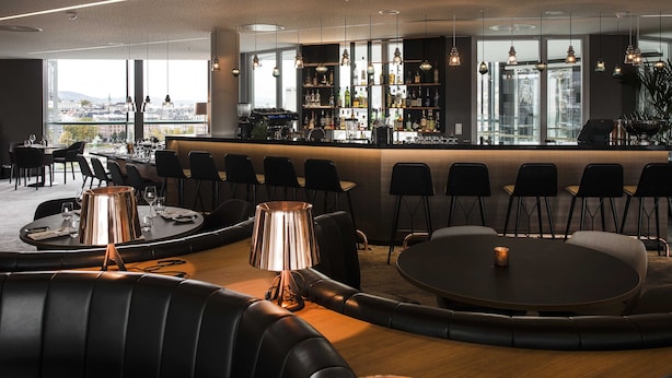 A modern bar area with a bar counter, seating, and a view of the city.