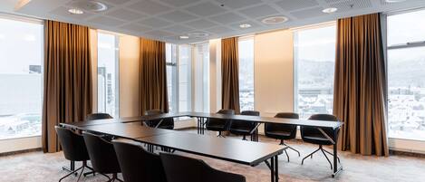 Une salle de conférence avec une longue table, de nombreuses chaises, de grandes fenêtres et une vue sur la ville.
