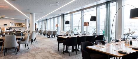 A modern dining area with long tables, chairs, and pendant lighting.