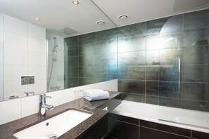 A modern bathroom with a large mirror, a sink, a bathtub, and a glass-enclosed shower.