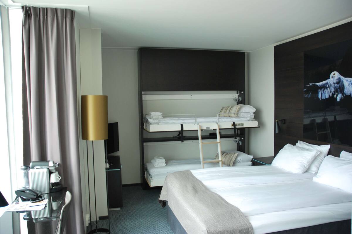 A hotel room with a bunk bed, a desk with a telephone, and a television.