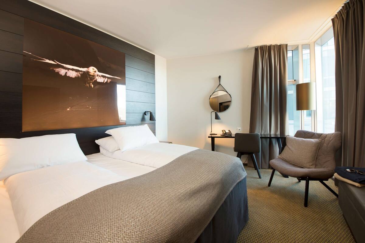A hotel room with a large bed, a desk, a chair, and a view of the city.