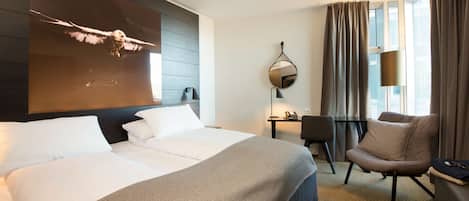 Ein Hotelzimmer mit zwei Betten, einem Schreibtisch, einem Stuhl und einem großen Fenster mit Vorhängen.