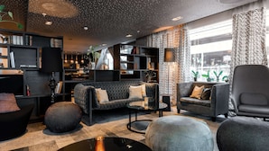 A modern living room with a sofa, armchairs, ottomans, and a coffee table. There are bookshelves and a TV on the wall.