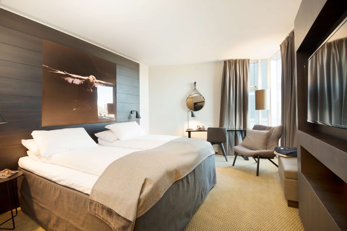 A hotel room with a large bed, a desk, a chair, a TV, and a mirror.
