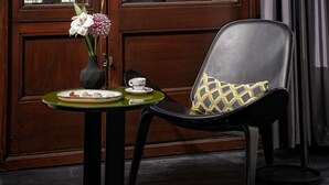 A room with a view of a historic building through large windows, a table with a vase of flowers, a chair with a patterned cushion, and a floor lamp. - art'otel Amsterdam (Amsterdam)