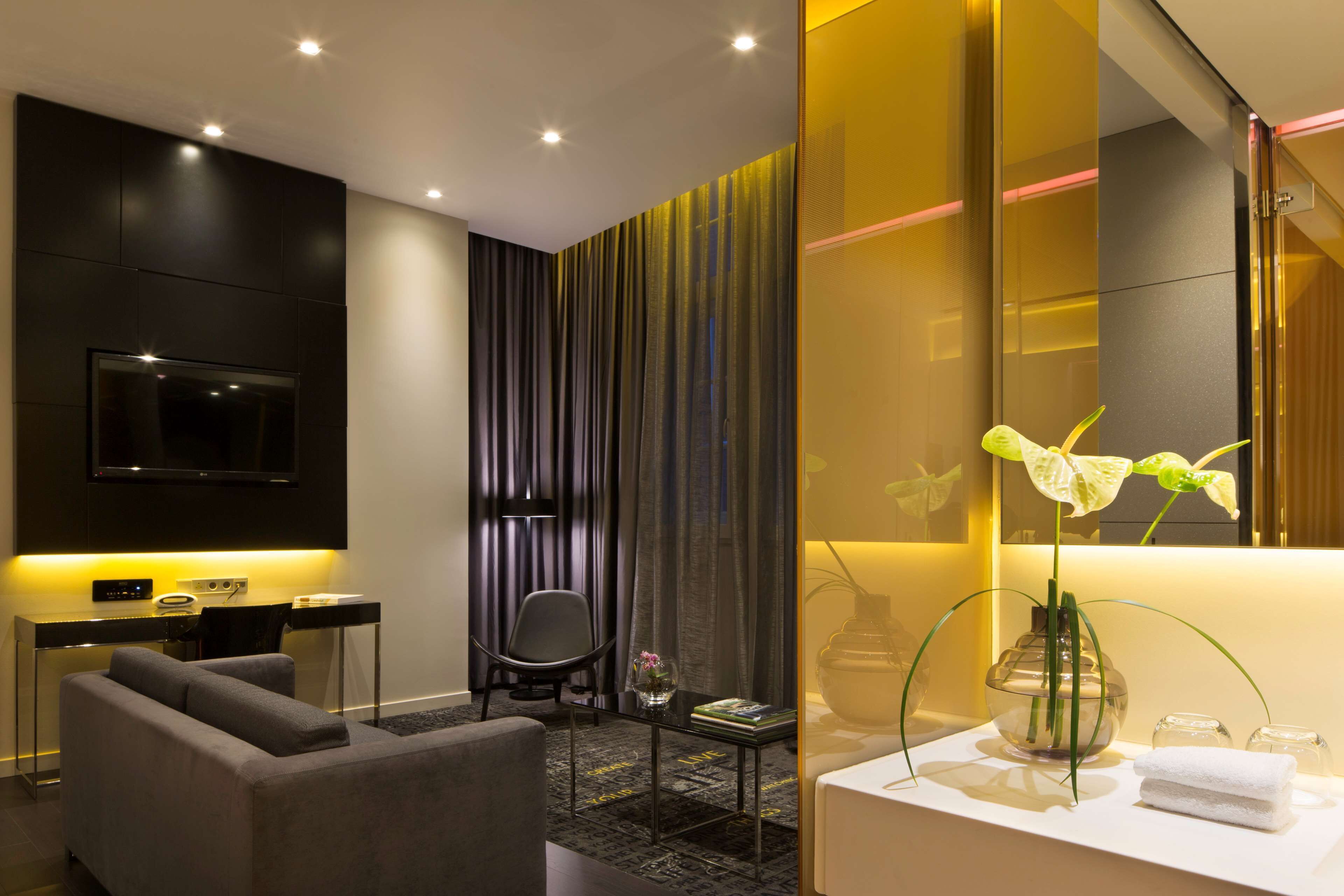 A modern hotel room with a flat-screen TV, a sofa, a desk, and a bathroom vanity.
