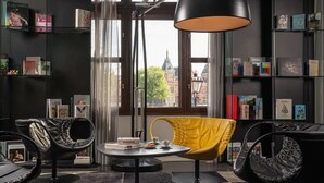 A modern reading room with leather chairs, a round table, and a large window overlooking a historic building. - art'otel Amsterdam (Amsterdam)