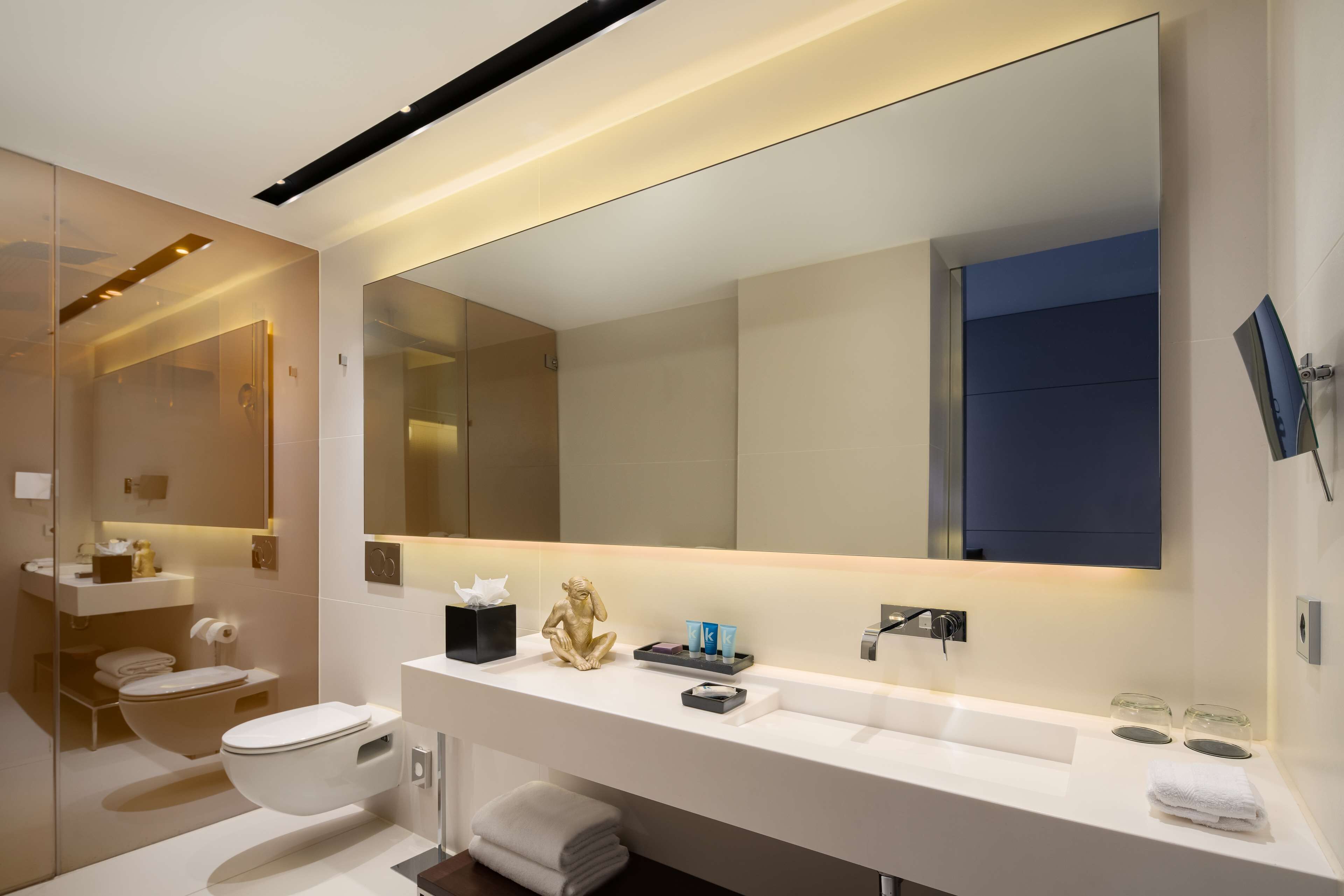 A modern bathroom with a large mirror, white vanity, and a toilet.