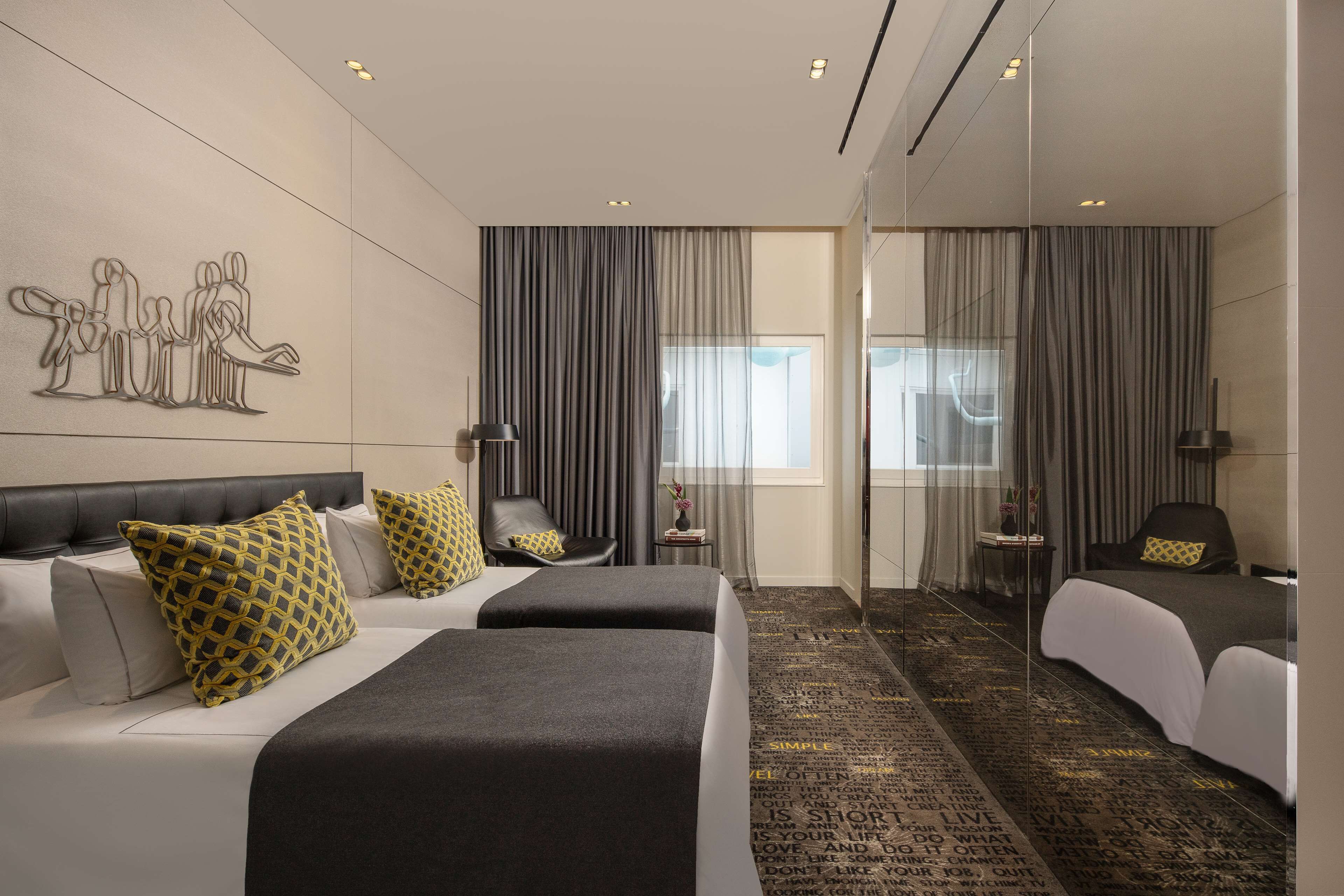 A modern hotel room with two beds, a large mirror, and a view of the city.