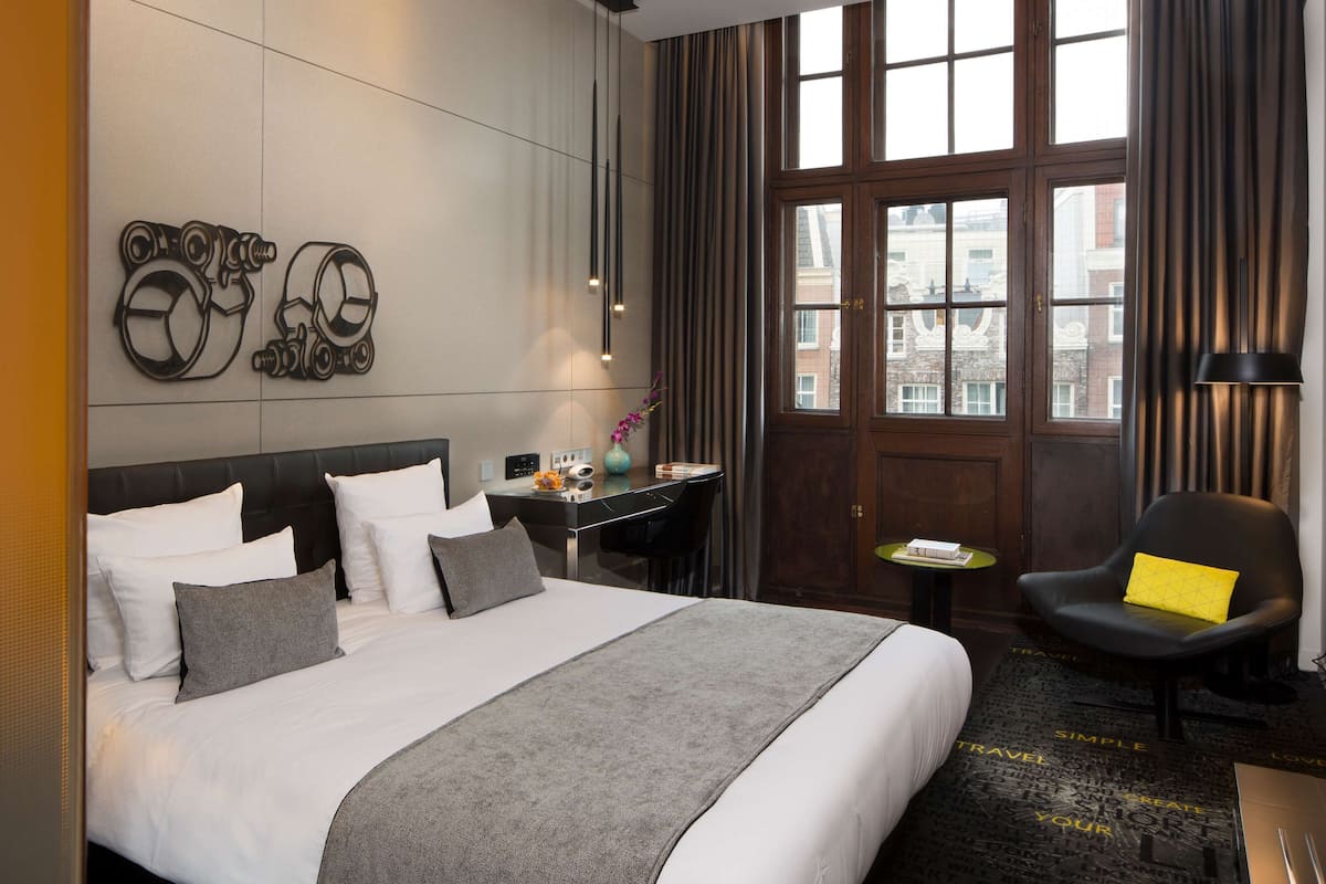Ein Hotelzimmer mit einem großen Bett, einem Schreibtisch, einem Stuhl und einem Vorhangfenster.