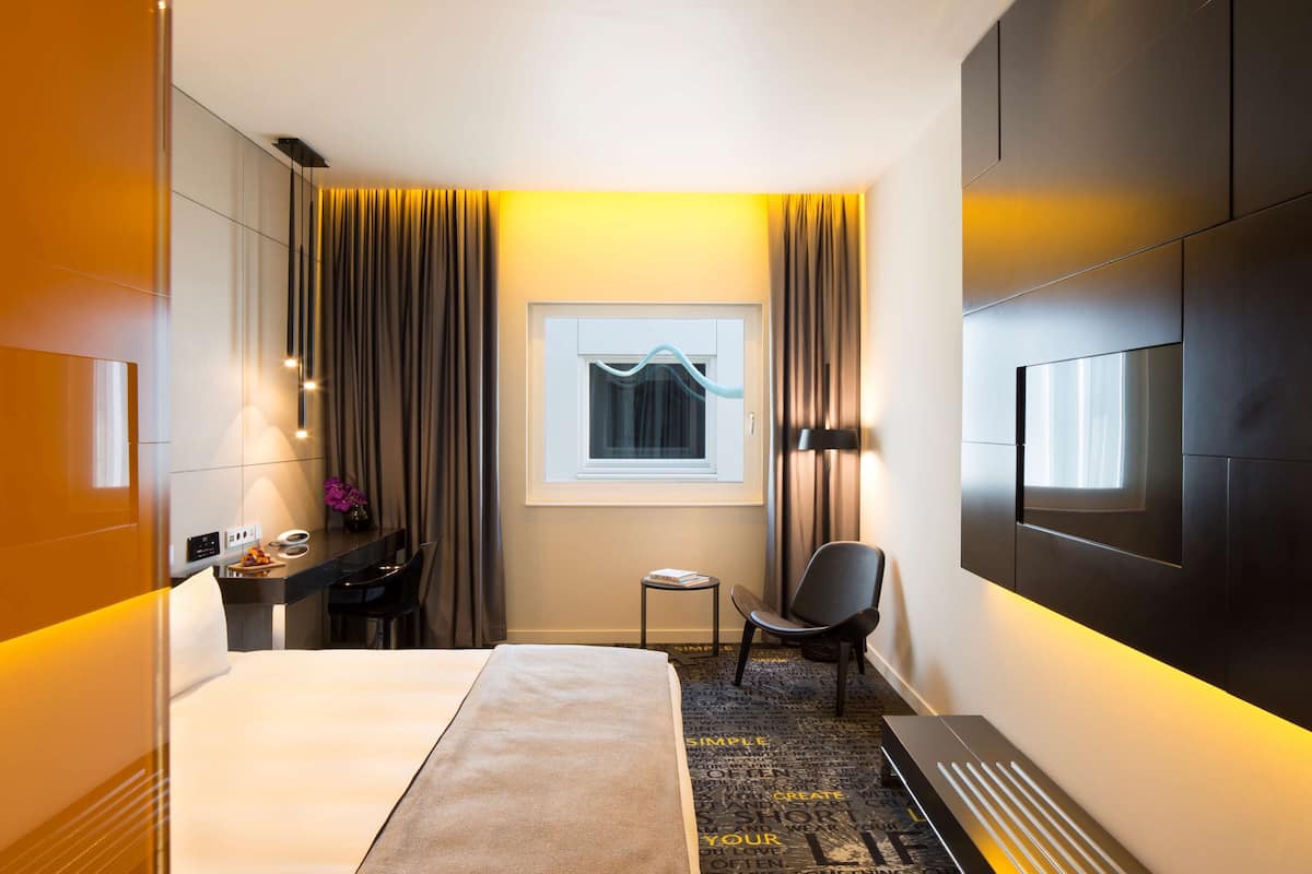 Ein modernes Hotelzimmer mit einem Bett, einem Schreibtisch, einem Sessel, einem kleinen Tisch und einem an der Wand befestigten Fernseher.