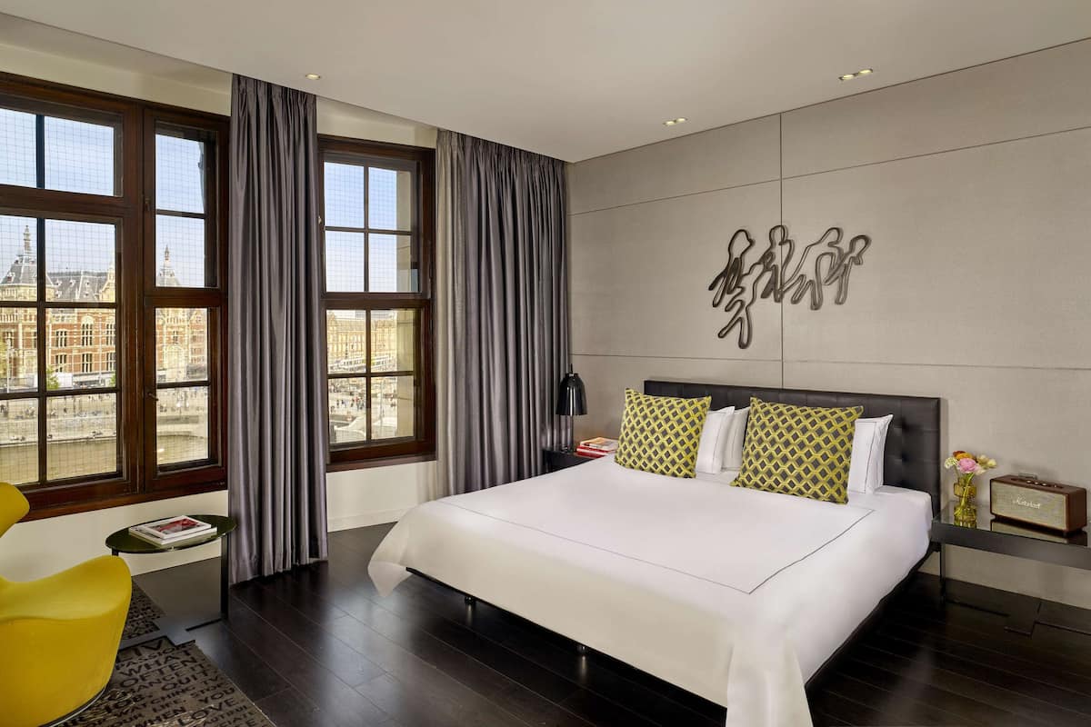 Ein modernes Hotelzimmer mit einem großen Bett, Blick auf ein historisches Gebäude und einem außergewöhnlichen Wandbild.