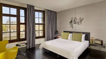 Quarto de hotel moderno com uma cama grande, vista para um edifício histórico e uma obra de arte original na parede.