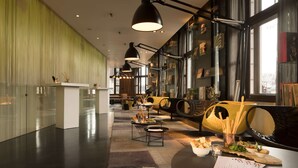 A modern interior with a reception desk, seating area with a wooden barrel, and a dining setup with a menu. - art'otel Amsterdam (Amsterdam)