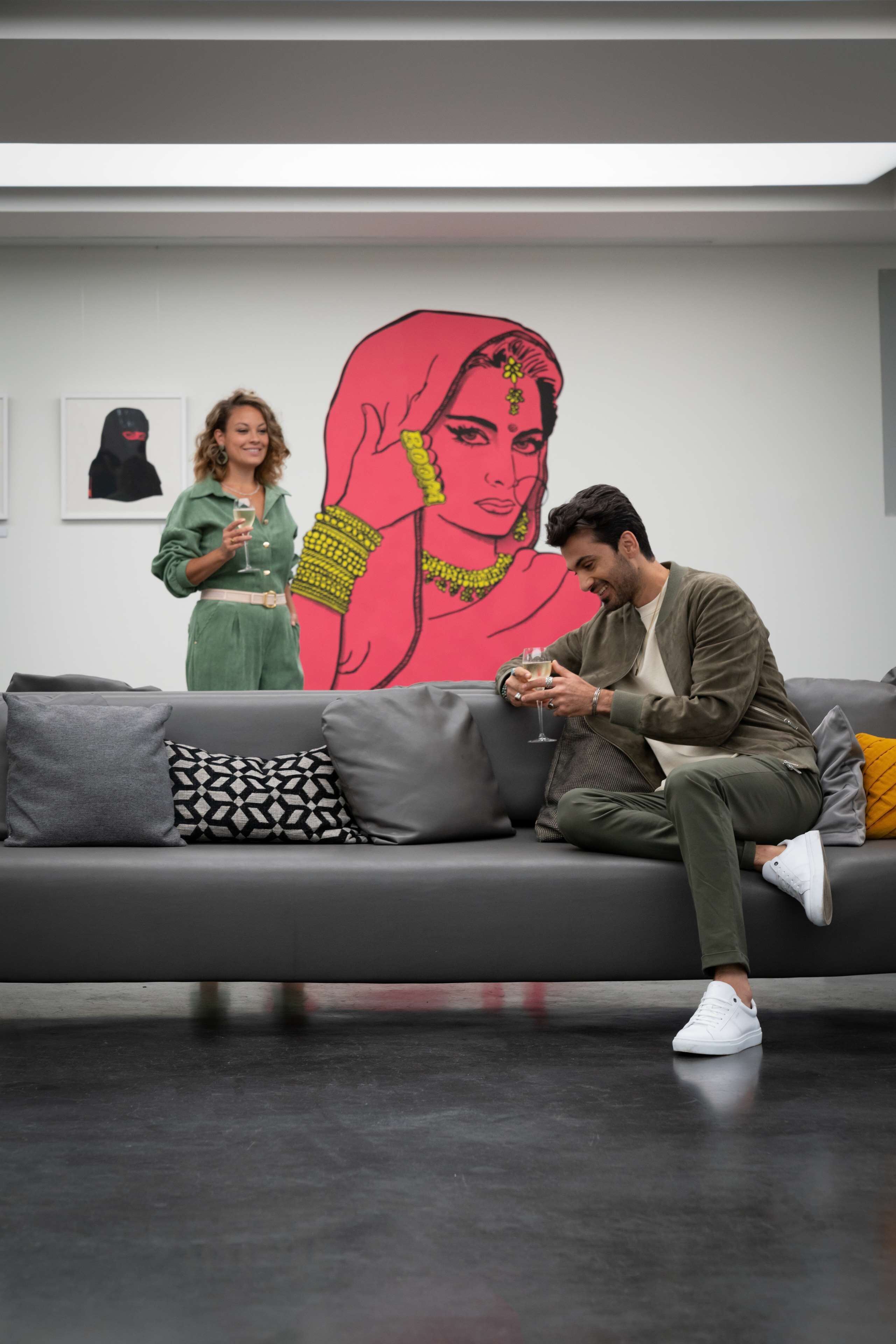 Two people on a grey sofa with a large red artwork in the background.