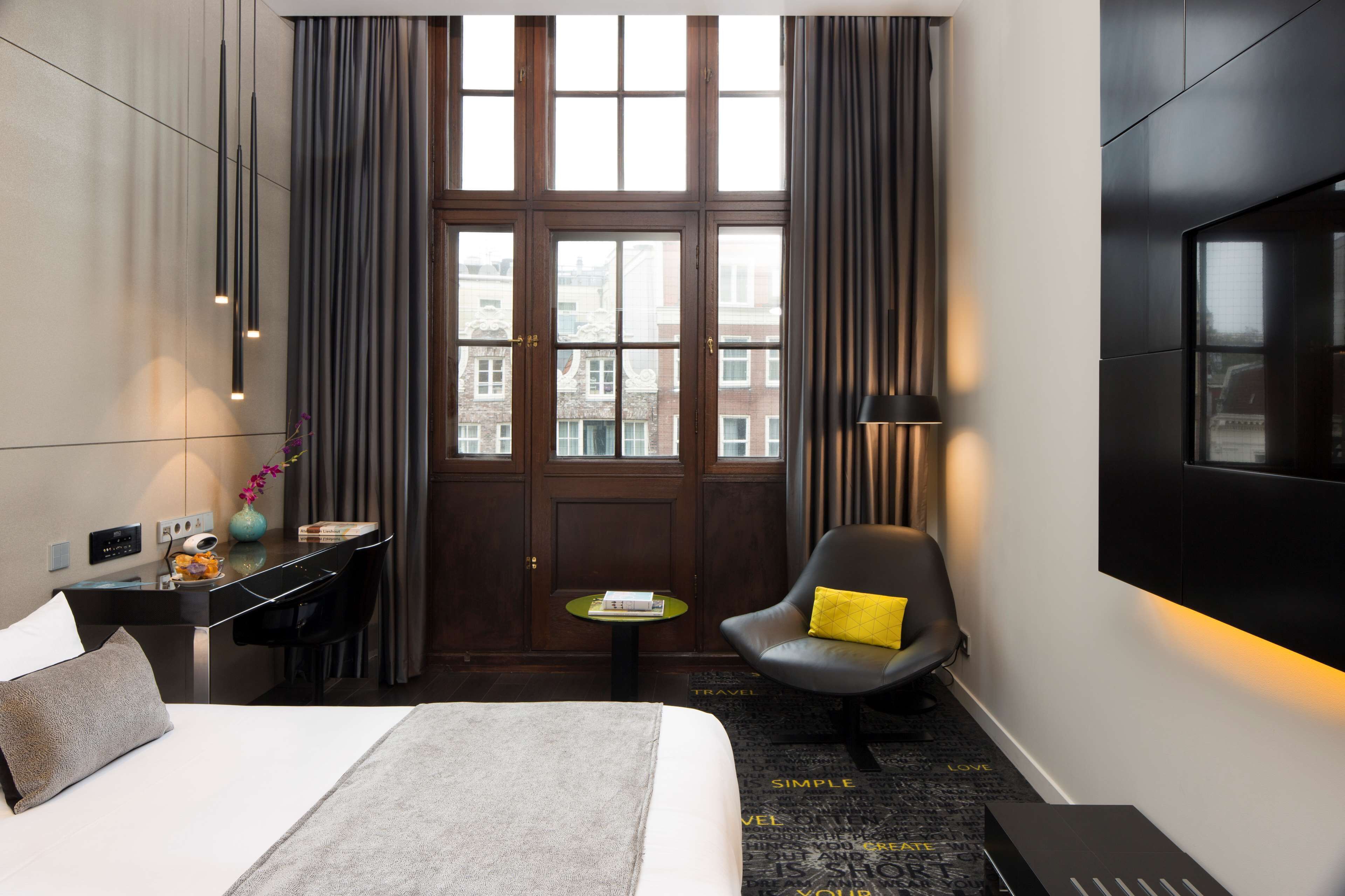 A hotel room with a bed, desk, chair, and a large window with curtains.