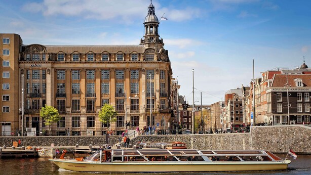 A historic building with a prominent clock tower, a waterfront, and a boat docked nearby. - art'otel Amsterdam (Amsterdam)
