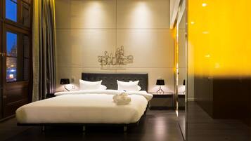 Ett modernt hotellrum med en stor säng, två sängbord, ett konstverk som hänger på väggen och utsikt över stadsbilden genom ett fönster.