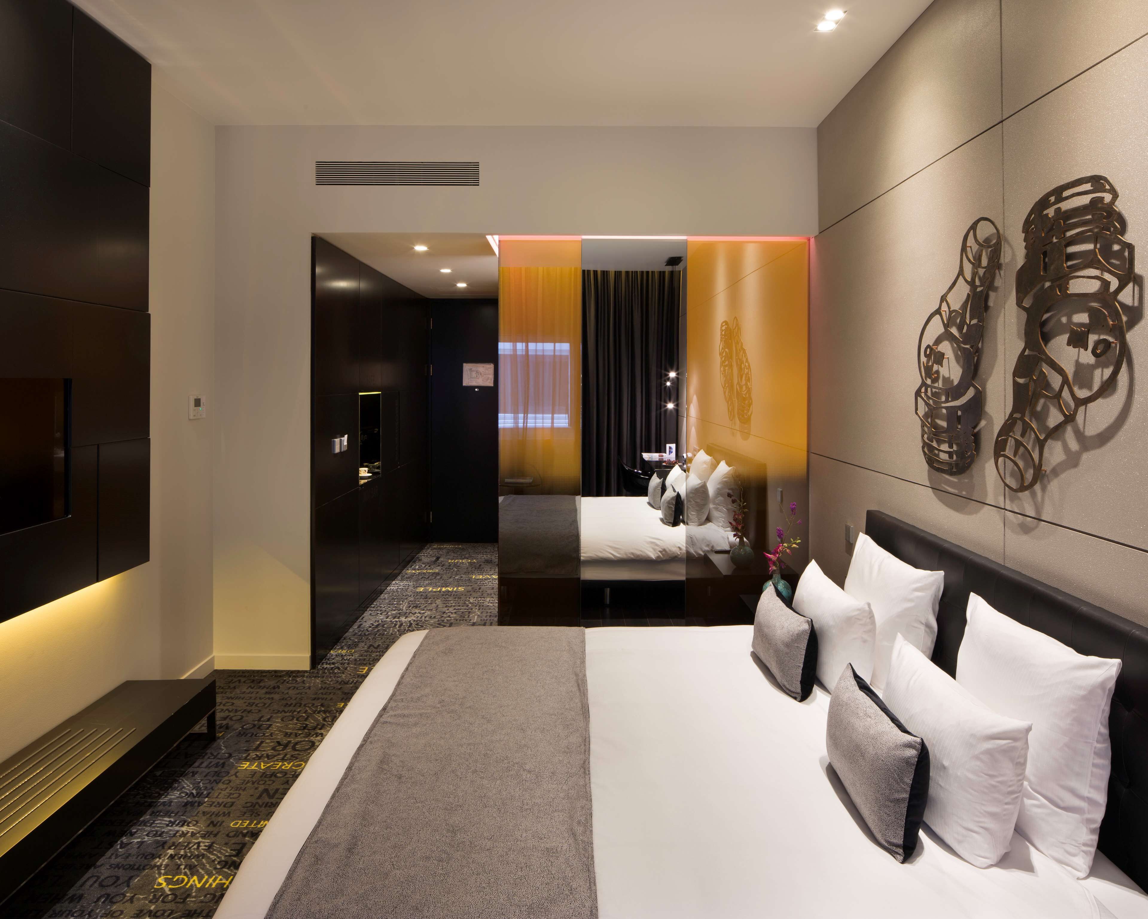 A modern hotel room with a large bed, a flat-screen TV, and a decorative wall piece.
