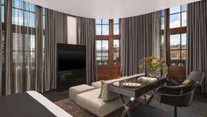 A modern hotel room with a large bed, a sofa, a desk, and a chair. There is a TV mounted on the wall and a window with curtains. - art'otel Amsterdam (Amsterdam)