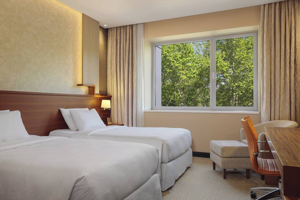 Une chambre d’hôtel avec deux lits, un bureau et une fenêtre donnant sur des arbres.
