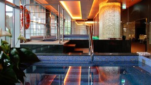Une piscine intérieure avec des parois en verre transparent, un comptoir d’accueil et un escalier menant aux niveaux supérieurs.