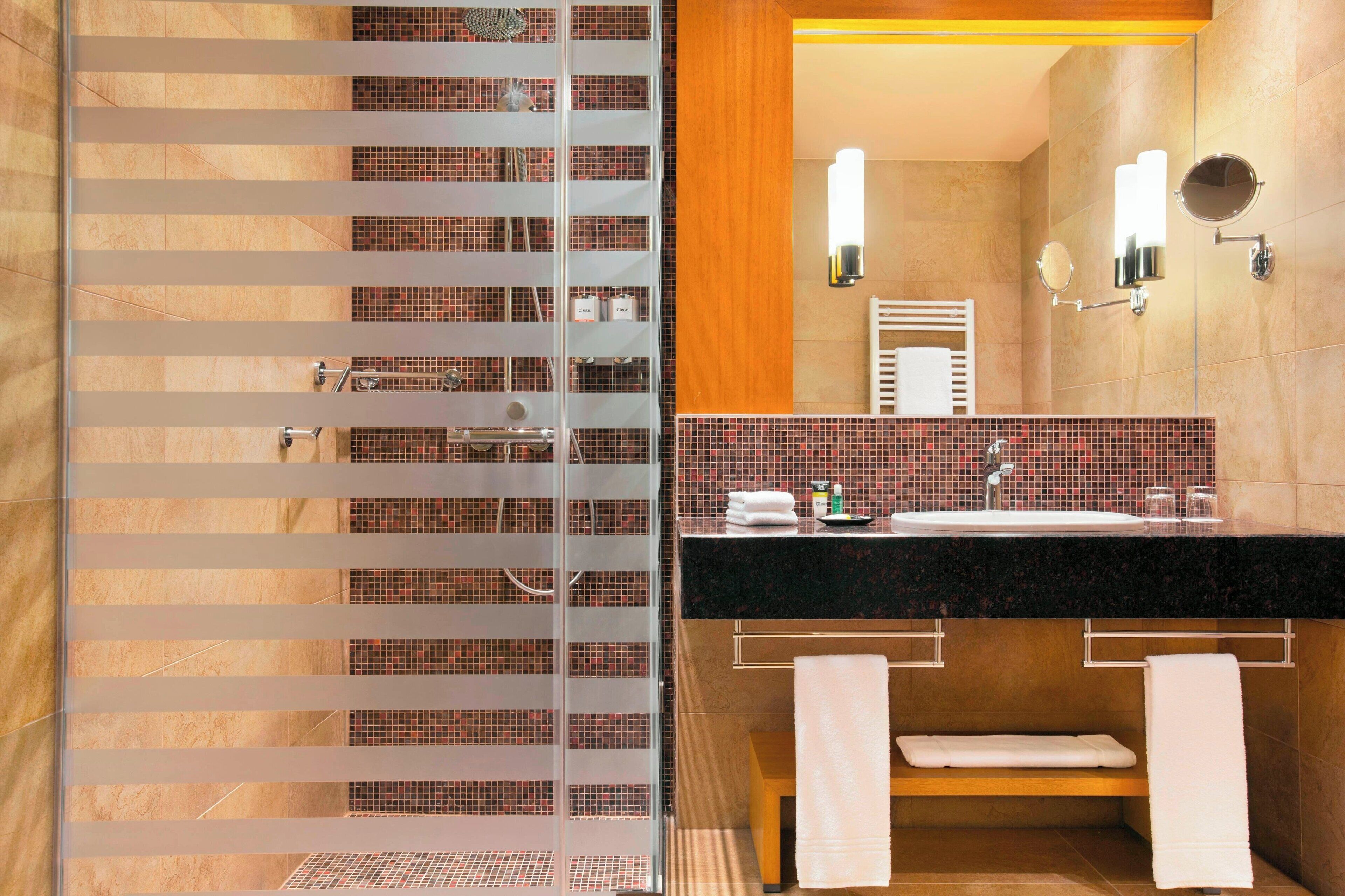 A modern bathroom with a glass shower enclosure, a black countertop sink, and two wall-mounted mirrors.