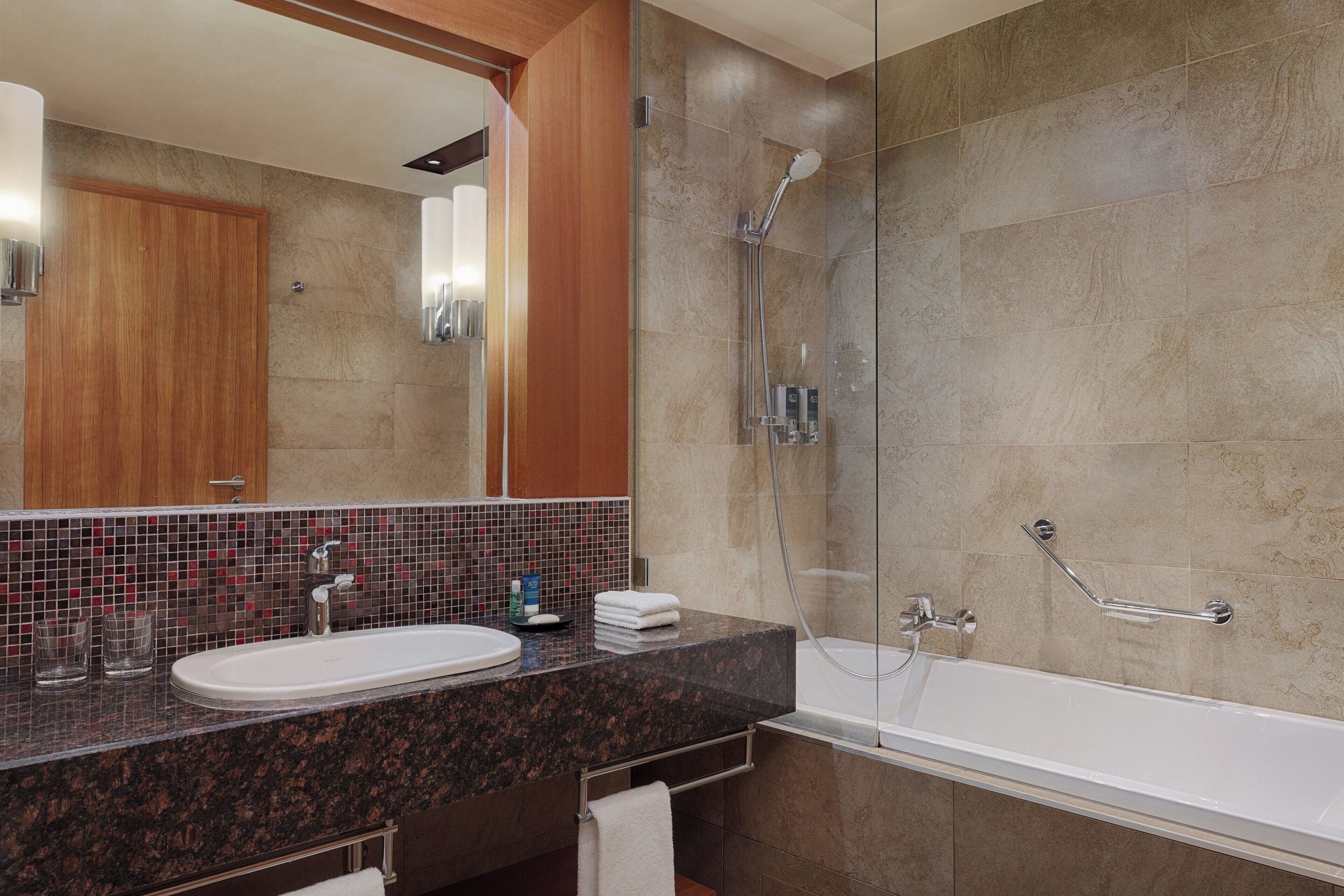 A modern bathroom with a granite countertop, a white sink, a glass-enclosed shower, and a wooden door.
