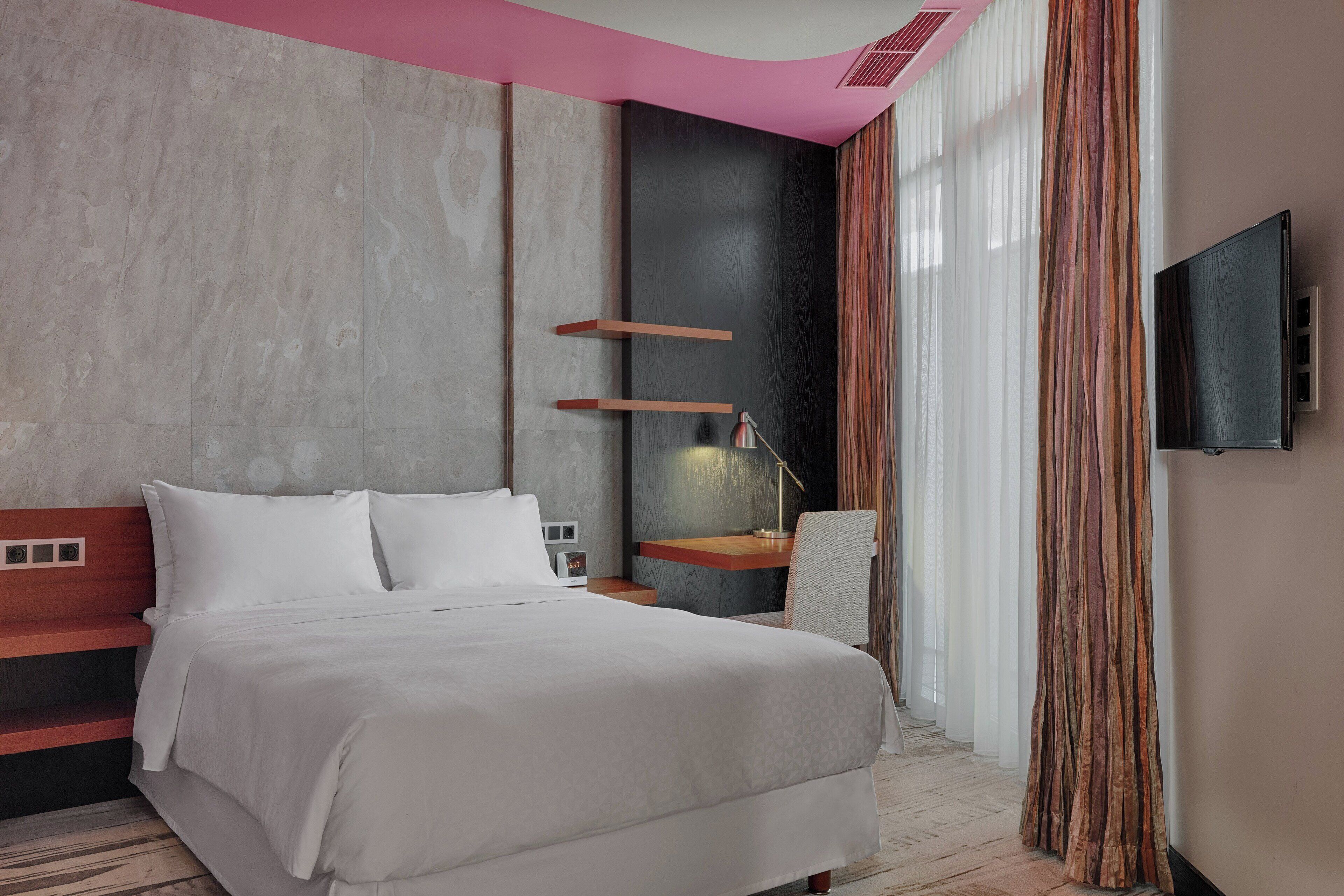 A modern hotel room with a large bed, a desk, and a TV mounted on the wall.