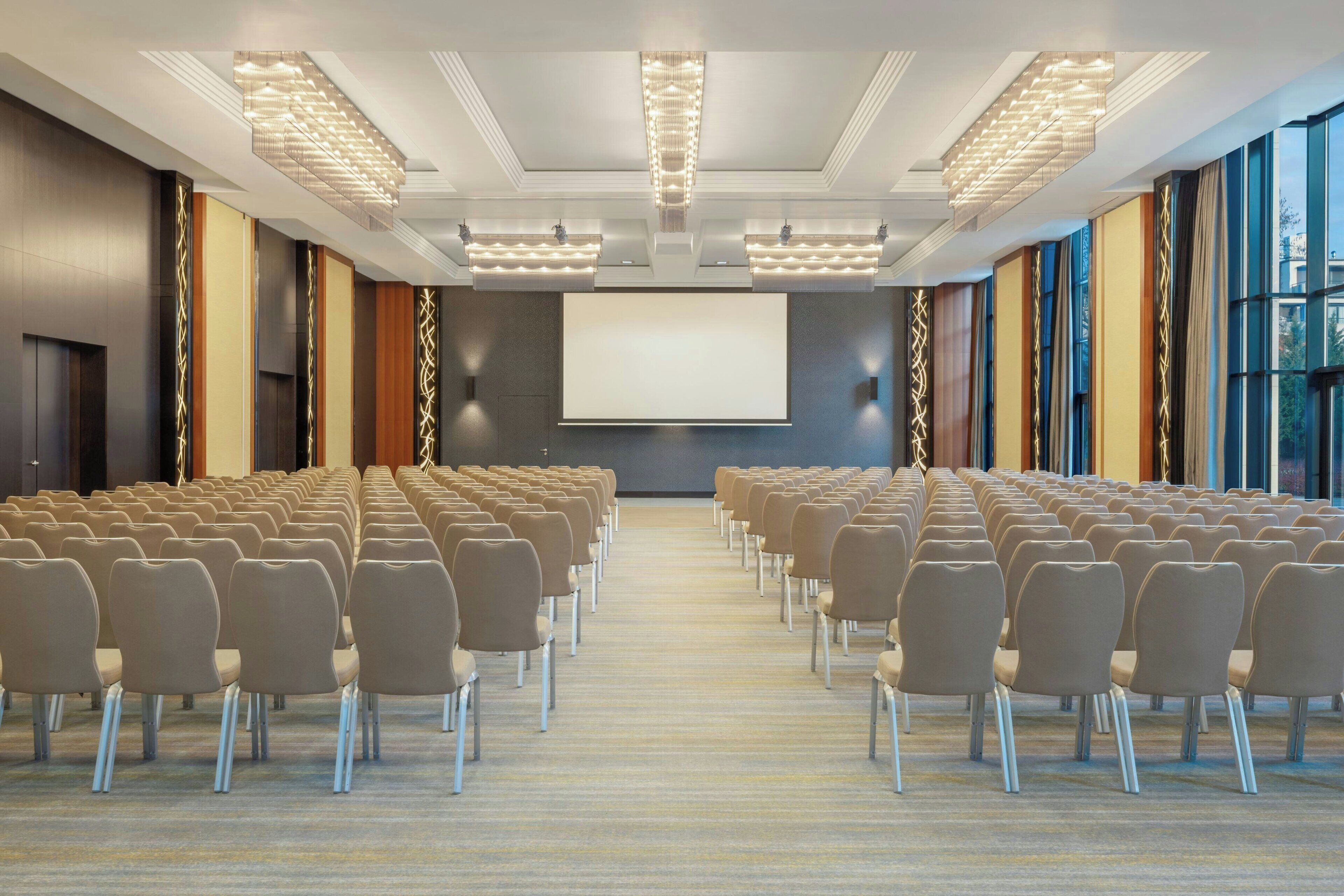 A conference room with rows of chairs, a large screen, and a modern ceiling design.