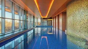 Une piscine intérieure moderne avec des rampes de protection en verre, un sol carrelé de bleu et un mur décoré de mosaïques.